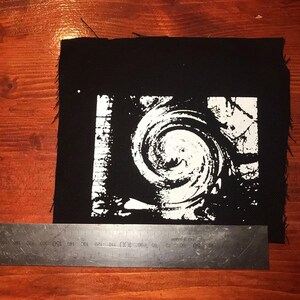 Puede incluir: Parche cuadrado negro con un dise&ntilde;o de espiral blanco. El parche mide aproximadamente 15 cm de ancho y 15 cm de alto. Los bordes est&aacute;n deshilachados. El dise&ntilde;o es un patr&oacute;n arremolinado.