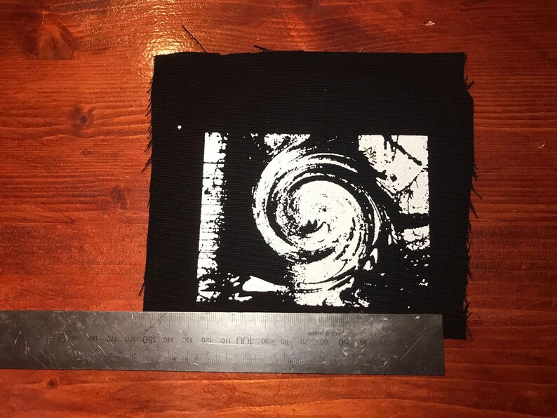 Puede incluir: Parche cuadrado negro con un dise&ntilde;o de espiral blanco. El parche mide aproximadamente 15 cm de ancho y 15 cm de alto. Los bordes est&aacute;n deshilachados. El dise&ntilde;o es un patr&oacute;n arremolinado.