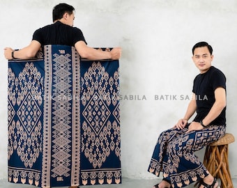 May include: Two men wearing a blue and brown patterned sarong. The sarong has a geometric design and the text "SABILA BATIK SABILA" is visible on the fabric.