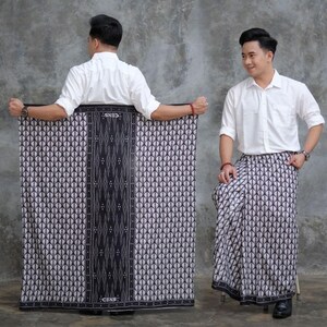 May include: A black and white patterned sarong, with a central dark vertical band. The sarong is worn by a person wearing a white button-down shirt. The sarong features a geometric design and the word "CENS" is visible.