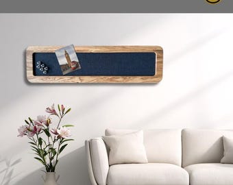 Puede incluir: Un tablón de anuncios magnético rectangular de madera con una inserción de tela azul oscuro. El tablón de anuncios tiene un marco de madera clara e incluye una postal y varios imanes pequeños. El texto "MAGNETISCHE PINNWAND EICHE" está en la parte superior.