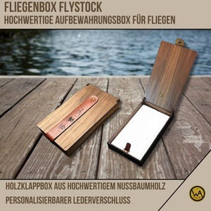 Może przedstawiać: Drewniana skrzynka do wędkowania muchowego z paskiem skórzanym i wygrawerowanym napisem "Fly Stock" na pokrywie. Skrzynka jest otwarta i pokazuje biały wkład z pianki. Skrzynka znajduje się na drewnianej powierzchni.
