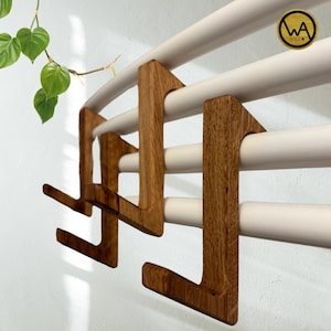 May include: Wooden wall mounted towel rack with four hooks. The rack is made of natural wood and has a light brown finish. The hooks are shaped like a letter L and are attached to the rack with screws.