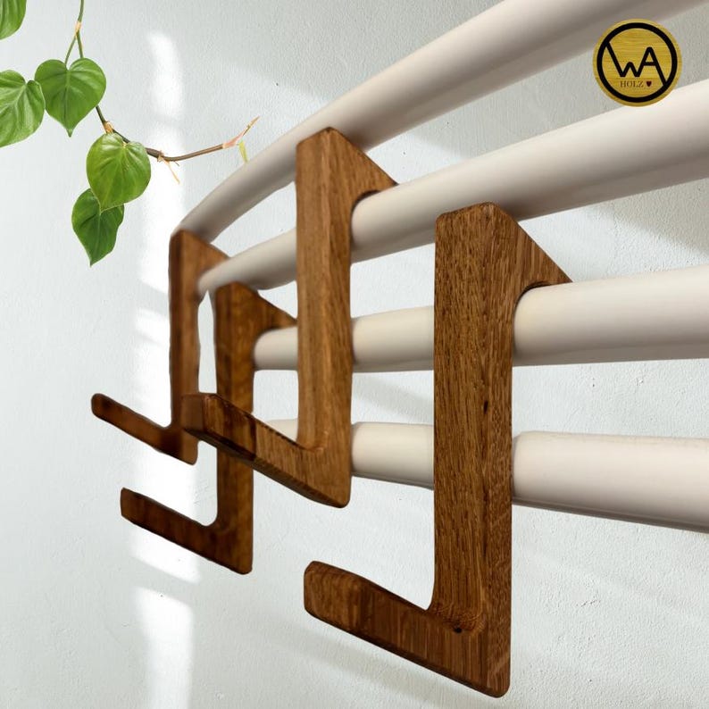 May include: Wooden wall mounted towel rack with four hooks. The rack is made of natural wood and has a light brown finish. The hooks are shaped like a letter L and are attached to the rack with screws.