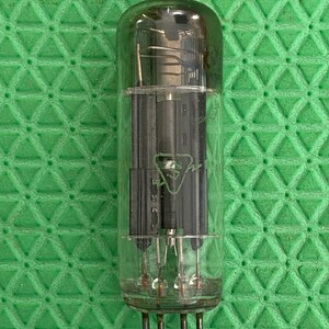 May include: A clear glass vacuum tube with internal components visible. The tube has a rounded top and several pins at the base. The internal components are dark and metallic. The tube is set against a green textured background.