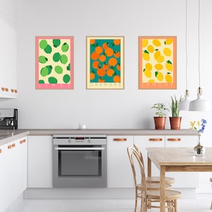 May include: Three framed prints of fruit illustrations. The prints are hung on a white wall in a kitchen. The prints feature limes, oranges, and lemons. The text below each print reads "Limes", "Oranges", and "Lemons".