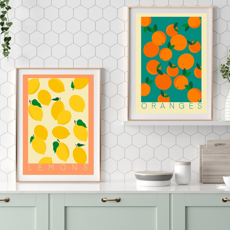 May include: Two framed prints with a white background and a light orange border. The print on the left features a yellow background with a pattern of lemons. The print on the right features a teal background with a pattern of oranges. The text "LEMONS" is at the bottom of the left print and the text "ORANGES" is at the bottom of the right print.