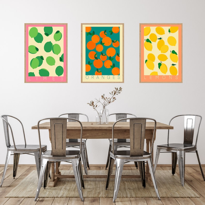 May include: Three framed prints of fruit illustrations. The top print is pink with green limes and the text "LIMES". The middle print is green with orange oranges and the text "ORANGES". The bottom print is orange with yellow lemons and the text "LEMONS".