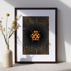 May include: A framed print with a black background and gold leaf design featuring a ladybug in the center.