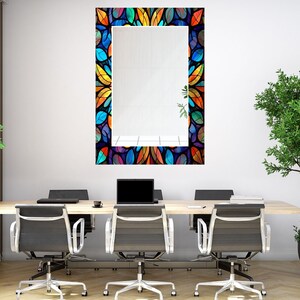 Peut inclure: Un miroir rectangulaire avec un cadre en vitrail color&eacute; pr&eacute;sentant un motif de feuilles dans des tons de bleu, vert, orange, jaune et violet. Le miroir est accroch&eacute; &agrave; un mur blanc dans un environnement de bureau.