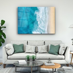 May include: An aerial view of a beach with turquoise water and white waves crashing on the shore. The sand is a light beige color.