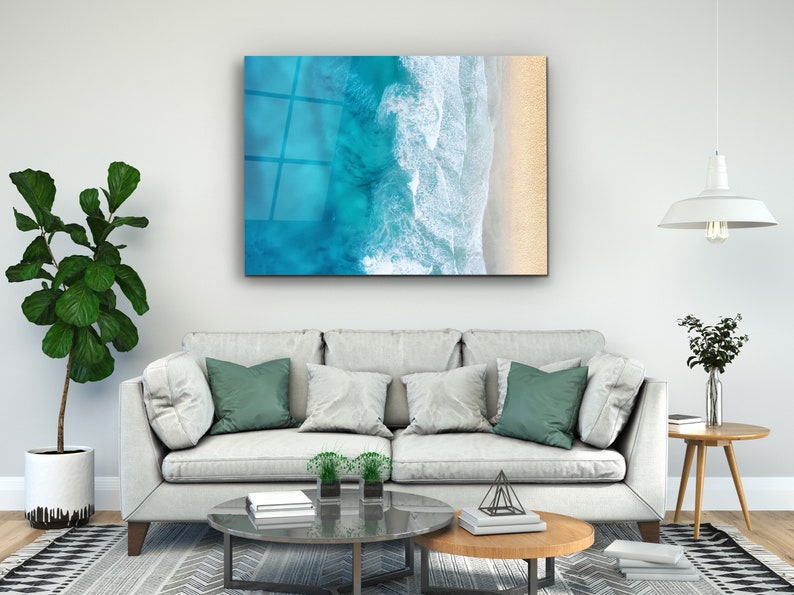 May include: An aerial view of a beach with turquoise water and white waves crashing on the shore. The sand is a light beige color.