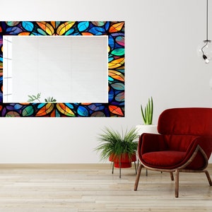 Peut inclure: Un grand miroir rectangulaire avec un cadre en vitrail color&eacute;. Le cadre pr&eacute;sente un motif r&eacute;p&eacute;titif de feuilles bleues, vertes, orange et jaunes. Le miroir est suspendu &agrave; un mur blanc au-dessus d'un fauteuil rouge.