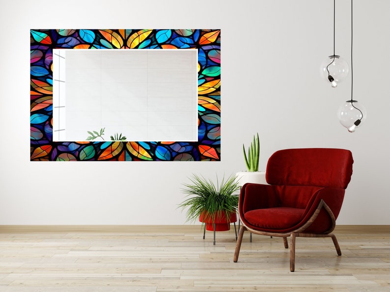 Peut inclure: Un grand miroir rectangulaire avec un cadre en vitrail color&eacute;. Le cadre pr&eacute;sente un motif r&eacute;p&eacute;titif de feuilles bleues, vertes, orange et jaunes. Le miroir est suspendu &agrave; un mur blanc au-dessus d'un fauteuil rouge.