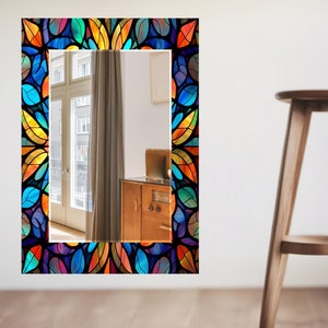 Peut inclure: Un miroir rectangulaire avec un cadre en verre color&eacute;. Le cadre pr&eacute;sente un motif de feuilles dans des tons de bleu, vert, jaune, orange et rouge. Le miroir refl&egrave;te une pi&egrave;ce avec une fen&ecirc;tre et un meuble en bois.