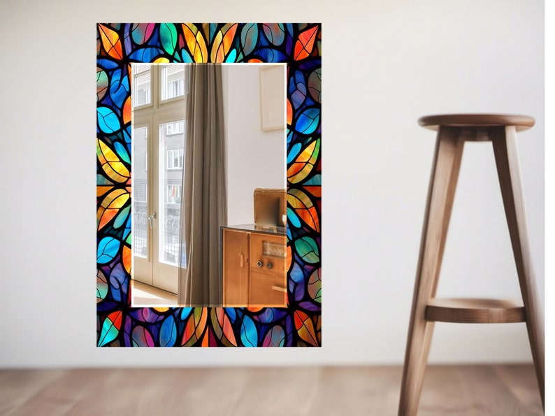 Peut inclure: Un miroir rectangulaire avec un cadre en verre color&eacute;. Le cadre pr&eacute;sente un motif de feuilles dans des tons de bleu, vert, jaune, orange et rouge. Le miroir refl&egrave;te une pi&egrave;ce avec une fen&ecirc;tre et un meuble en bois.