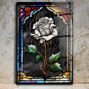 May include: A white rose with green leaves and a gold stem is depicted in a stained glass window. The window is framed with colorful glass pieces in shades of blue, red, yellow, and purple.