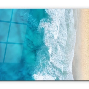 May include: An aerial view of a sandy beach with turquoise blue ocean water and white foamy waves crashing on the shore.