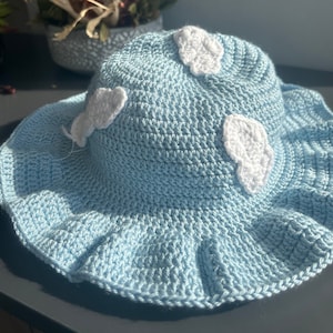 May include: A light blue crocheted sun hat with white crocheted clouds.