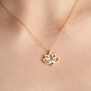 Peut inclure: Un collier en chaîne dorée avec un pendentif délicat en forme de fleur de lotus orné d'une petite pierre précieuse verte au centre.
