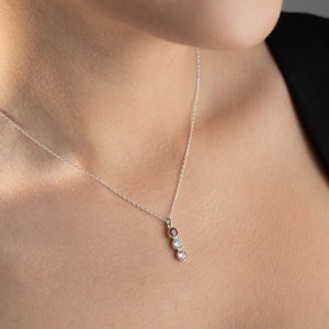 May include: A silver necklace with a pendant featuring three small round gemstones in shades of pink, white, and purple.