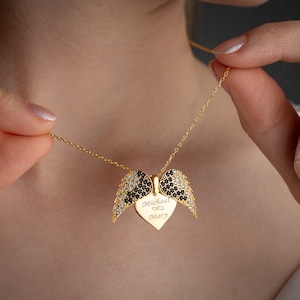 Puede incluir: Collar de oro con un colgante en forma de corazón adornado con piedras de circonita cúbica negras y blancas. El corazón tiene la inscripción "Micheal ∞ Mary". El colgante tiene forma de alas de ángel.