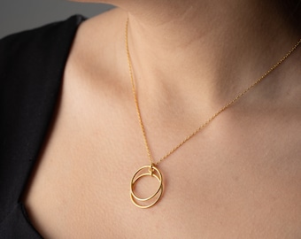 Könnte beinhalten: Eine goldene Halskette mit einem Doppelkreis-Anhänger. Die Kette ist zart und schlicht, was sie zu einem perfekten Alltagsstück macht.