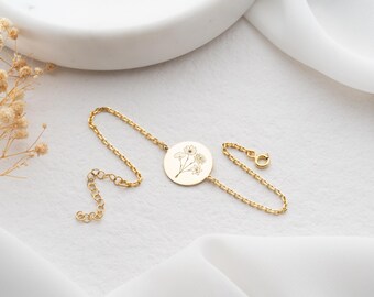 May include: A gold chain bracelet with a round pendant featuring a delicate floral design.