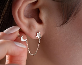 Op de afbeelding: Zilveren oorhangers met een ster- en maanontwerp. De ster-oorbel is met een fijne ketting verbonden met de maan-oorbel. De oorbellen worden op het oor gedragen.