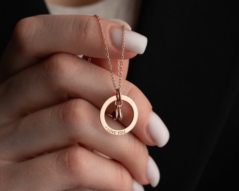 Hand holding a personalized necklace with a ring that reads “I love you”