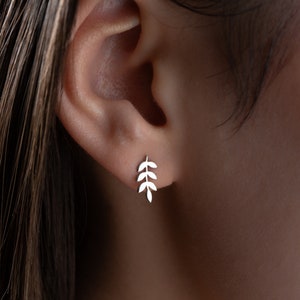 May include: A close-up of a person's ear with a silver leaf-shaped earring. The earring is a delicate design with multiple leaves.