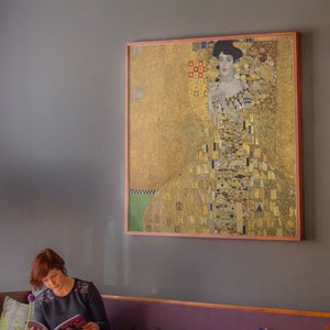May include: A framed painting of a woman in a gold dress with a geometric pattern. The painting is set against a gray wall.