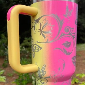 May include: A pink and yellow stainless steel travel mug with a yellow handle. The mug has a silver butterfly design with floral accents.