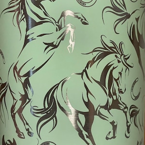 May include: A light green tumbler with a repeating pattern of rearing horses and horseshoes in a metallic silver color. The horses are depicted in a stylized, artistic manner, creating a dynamic and eye-catching design. The tumbler is likely designed for cold beverages.