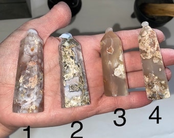 May include: Four agate crystal points, numbered 1 through 4, are displayed on a hand. The points are all different shades of brown, white, and gray.