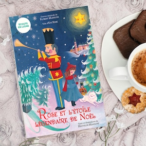 Peut inclure: Un livre pour enfants intitulé "Rose et l'Étoile Légendaire de Noël" avec des illustrations d'un casse-noisette, d'une fille et d'un sapin de Noël. Le livre est à côté d'une tasse de café, de biscuits et d'une assiette blanche.