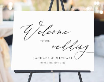 以下が含まれることがあります： 黒い書道で「ようこそ、私たちの結婚式へ  Rachael & Michael 2022年9月24日」と書かれた白い結婚式のウェルカムサイン。サインは黒いイーゼルに置かれています。