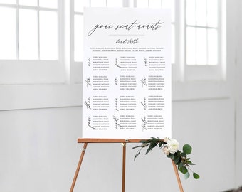 以下が含まれることがあります： 「your seat awaits」の文字が書かれた白い席次表。木製のイーゼルに飾られ、花の装飾が施されています。「bert table」という見出しの下に名前がリストされています。