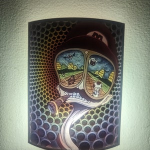 May include: A nightlight with a colorful image of a cartoon character wearing goggles and a hat. The character is surrounded by a psychedelic pattern of circles.