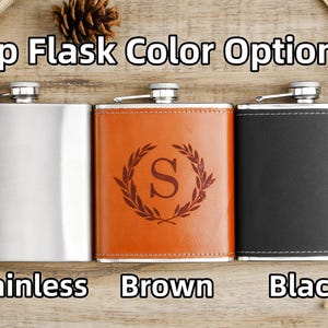 Könnte beinhalten: Drei Hüftflaschen in verschiedenen Farben: Edelstahl, braunes Leder und schwarzes Leder. Jede Flasche hat einen silbernen Verschluss und ein eingraviertes Initial „S“ auf der Vorderseite. Der Text „Hip Flask Color Options“ befindet sich oben im Bild.