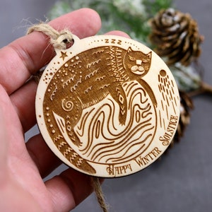 May include: A wooden ornament with a cat sleeping on a moon with the text "Happy Winter Solstice" and "zzz" around the cat.