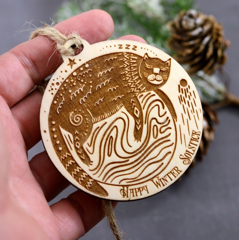 May include: A wooden ornament with a cat sleeping on a moon with the text "Happy Winter Solstice" and "zzz" around the cat.