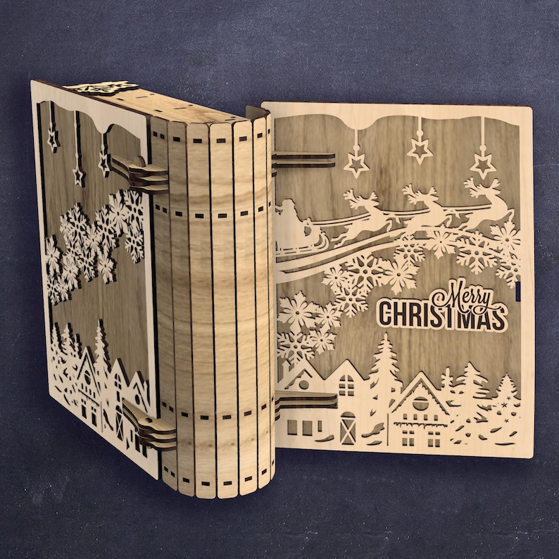 Peut inclure: D&eacute;coration en bois en forme de livre sur le th&egrave;me de No&euml;l. Le livre ouvert r&eacute;v&egrave;le un motif d&eacute;coup&eacute; au laser d'un village d'hiver, de flocons de neige, d'&eacute;toiles et du tra&icirc;neau du P&egrave;re No&euml;l. Les mots "Merry Christmas" sont &eacute;galement visibles.