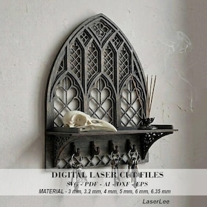 May include: A gray, laser-cut wooden wall shelf in a gothic window design. It features a shelf, key hooks, and a decorative top. The shelf holds a bird skull and incense. Text on the image reads "DIGITAL LASER CUT FILES".