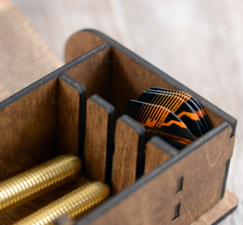 May include: A wooden box with multiple compartments for storing darts. The box is made of dark wood with black accents. The box is open and you can see a stack of orange and black darts inside.