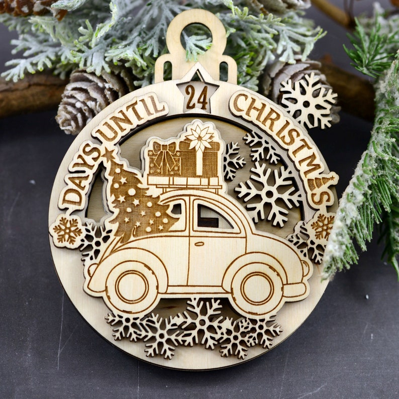 Puede incluir: Un adorno de madera para la cuenta atr&aacute;s de Navidad con un coche que lleva un &aacute;rbol de Navidad y regalos. El adorno est&aacute; decorado con copos de nieve y el texto "Days Until Christmas".