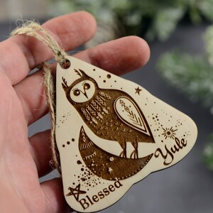 May include: A wooden Christmas ornament shaped like a triangle with a brown owl design and the words "Blessed Yule" on it.