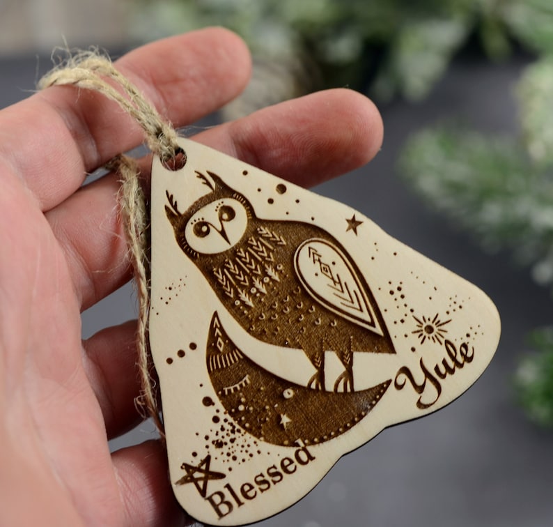 May include: A wooden Christmas ornament shaped like a triangle with a brown owl design and the words "Blessed Yule" on it.