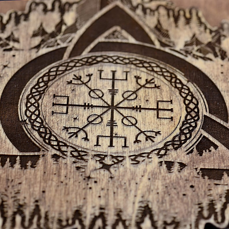 May include: A wooden sign with a black and white compass design surrounded by a Celtic knot. The compass is a Vegvisir, a Norse symbol for guidance and protection. The background is a wood grain pattern with a forest scene.