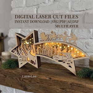 Op de afbeelding: Een meerlaagse, stervormige kerstdecoratie van hout met een lasergesneden tafereel van een huis, een hert, een auto met een boom en de kerstman in een arrenslee. De tekst luidt DIGITAL LASER CUT FILES INSTANT DOWNLOAD |SVG|PDF|AI|DXF MULTILAYER.